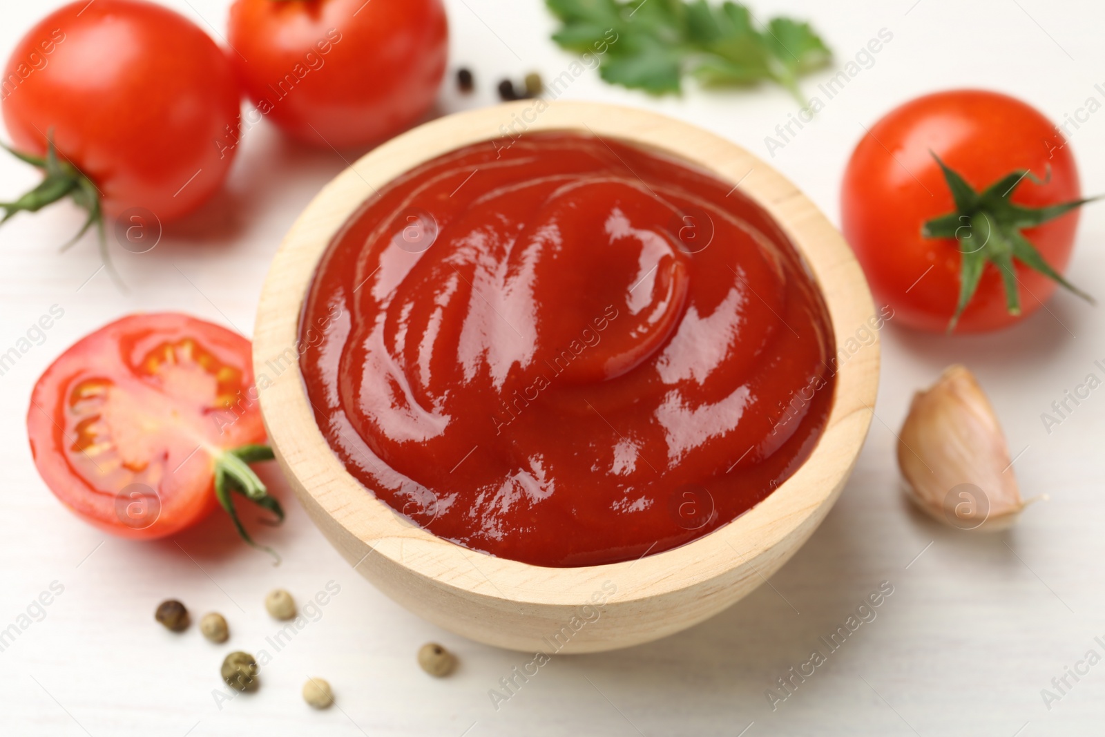 Photo of Delicious ketchup in bowl, garlic and tomatoes on white wooden table, closeup