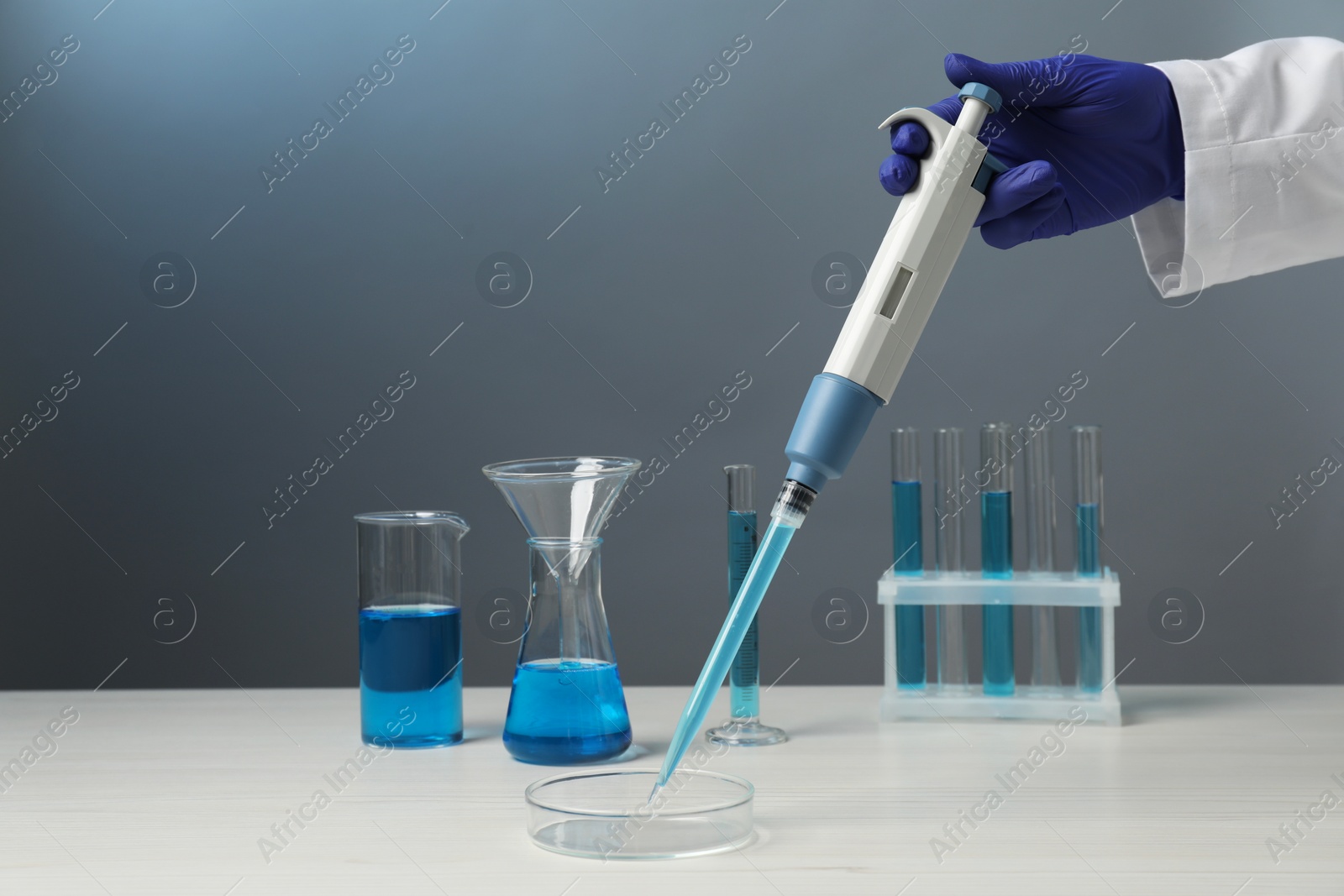 Photo of Laboratory analysis. Scientist dripping sample with micropipette into petri dish at white wooden table, closeup