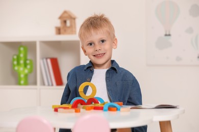 Photo of Cute little boy playing with colorful wooden pieces at white table indoors. Child's toy