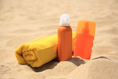 Photo of Sunscreens and rolled towel on sandy beach. Sun protection