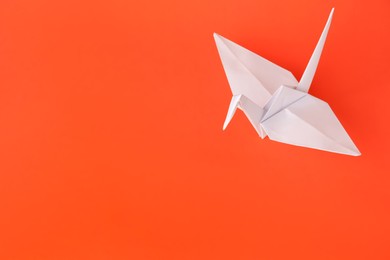 Photo of Origami art. Handmade paper crane on orange background, above view. Space for text