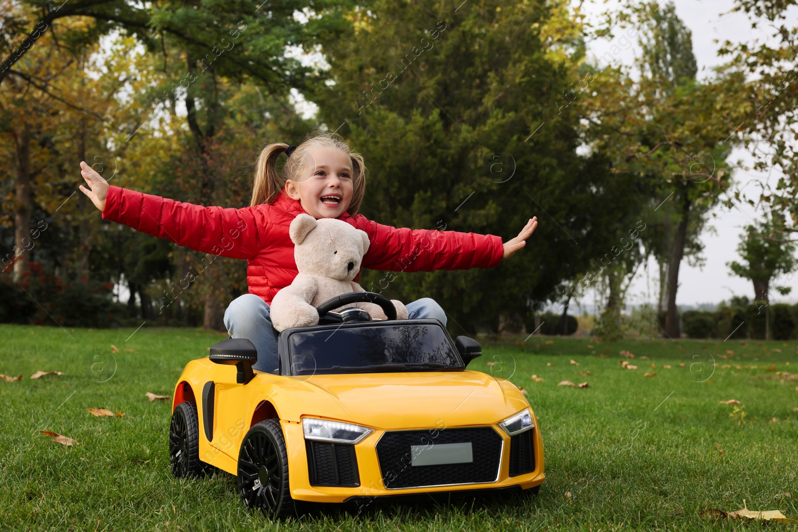 Photo of Cute little girl playing with toy bear and children's car in park. Space for text