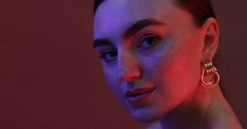 Portrait of beautiful young woman on color background in neon lights, closeup. Space for text