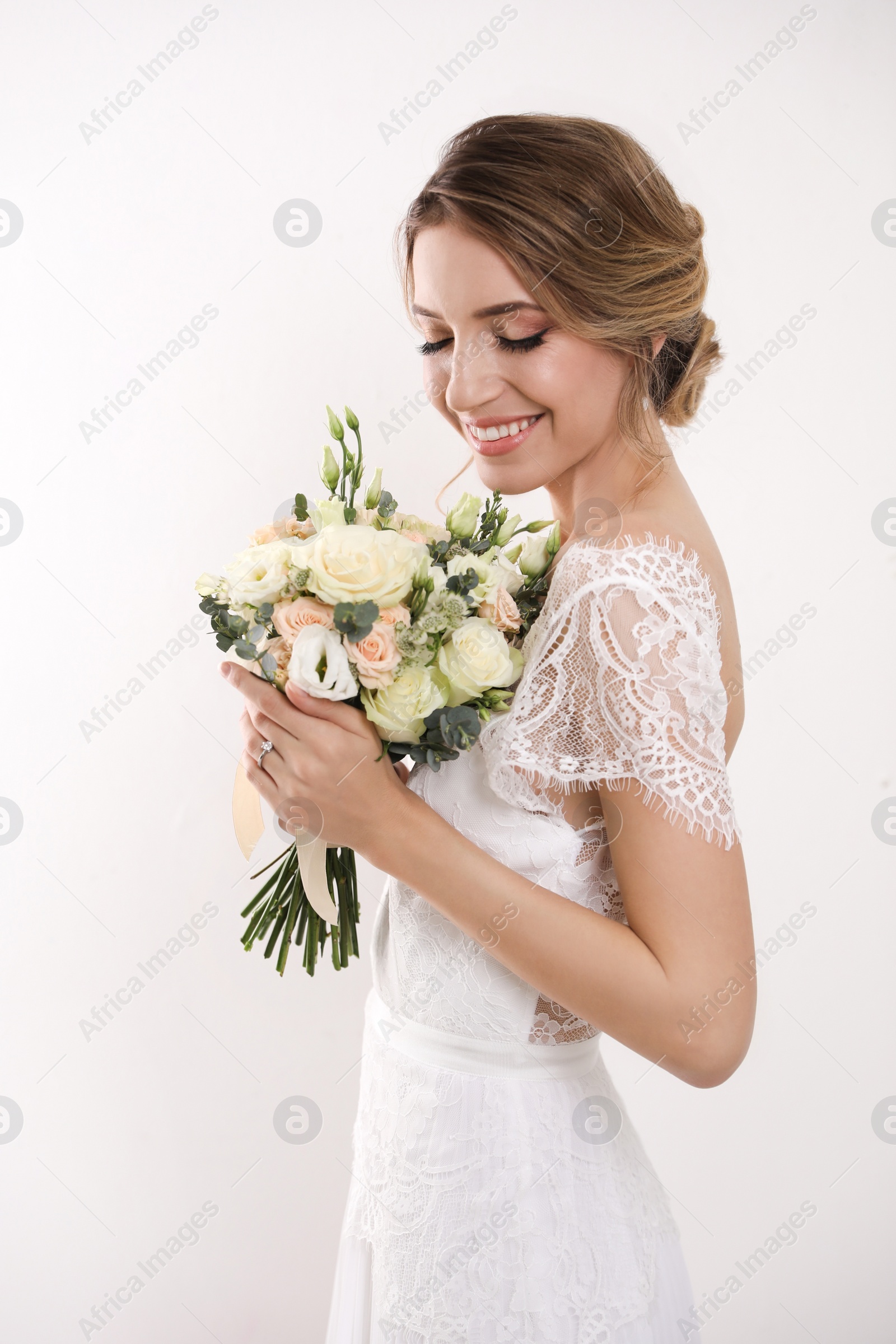 Photo of Young bride with elegant hairstyle holding wedding bouquet on white background