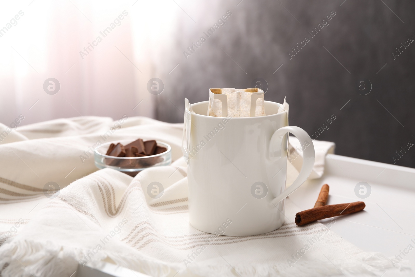 Photo of Cup with drip coffee bag and cinnamon on white table, closeup