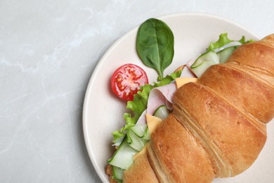 Photo of Tasty croissant sandwich with ham and cucumber on light grey marble table, top view