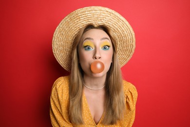 Photo of Fashionable young woman with bright makeup blowing bubblegum on red background