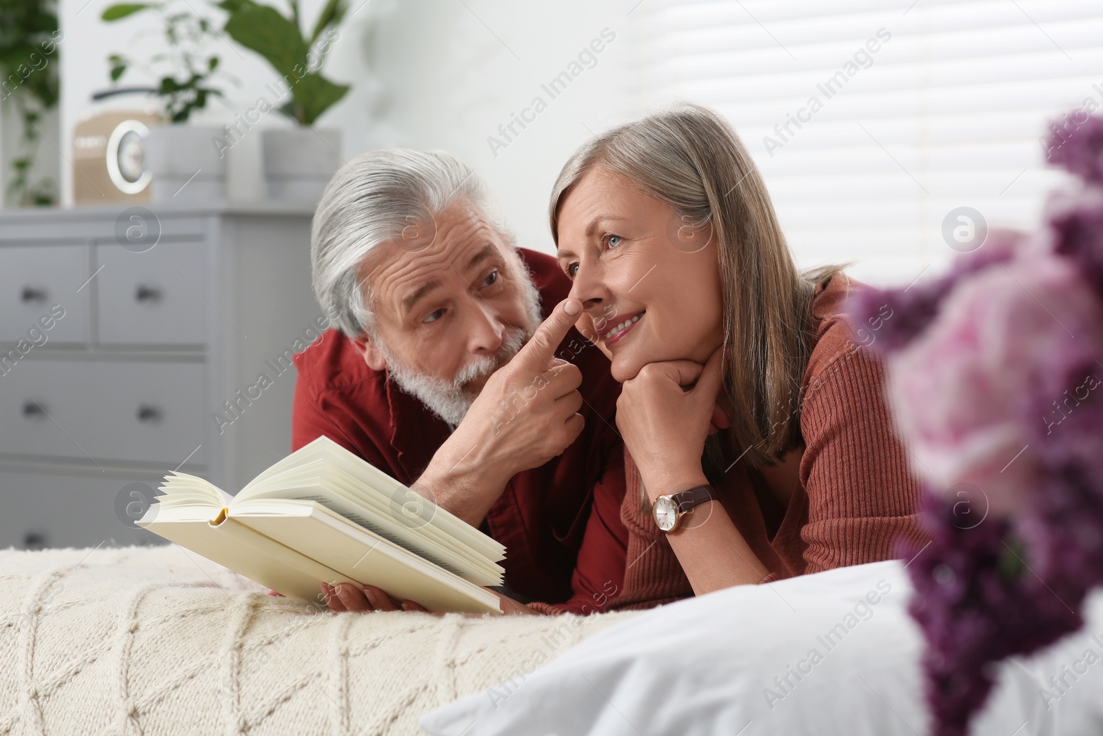 Photo of Lovely senior couple reading book on bed at home