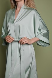 Photo of Woman in beautiful light green silk robe on olive background, closeup
