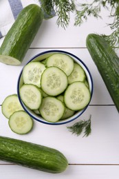 Photo of Cut cucumber in bowl, fresh vegetables and dill on white wooden table, flat lay