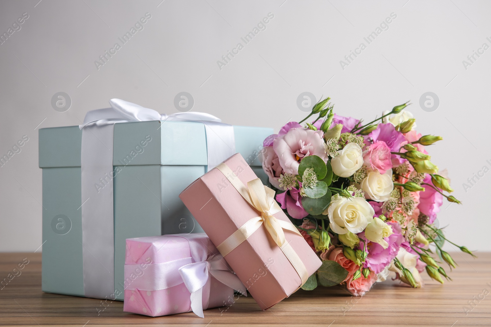 Photo of Beautiful bouquet of flowers and gift boxes on wooden table against light background