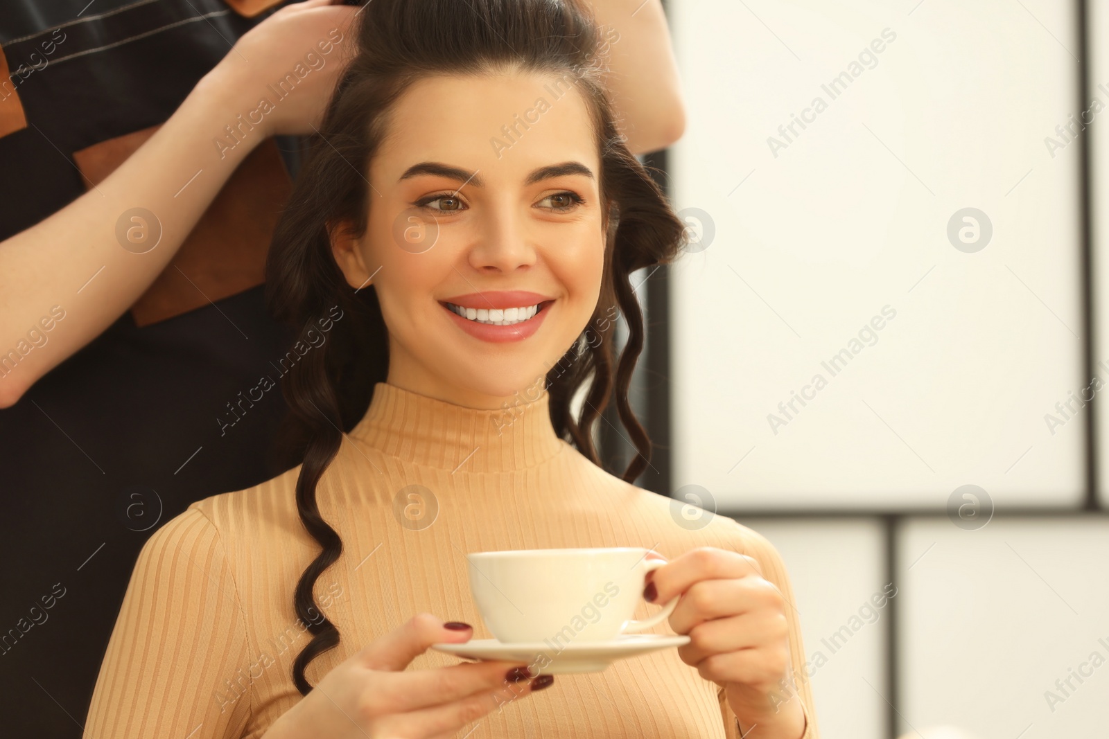 Photo of Hair styling. Professional hairdresser working with smiling woman while she drinking coffee in salon, closeup. Space for text