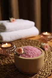 Photo of Bowl of pink sea salt, roses, burning candles and towels on wooden table