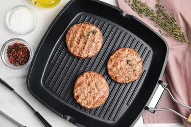 Photo of Grill pan with tasty fried hamburger patties and seasonings on white marble table, flat lay