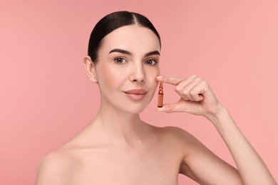 Photo of Beautiful young woman holding skincare ampoule on pink background