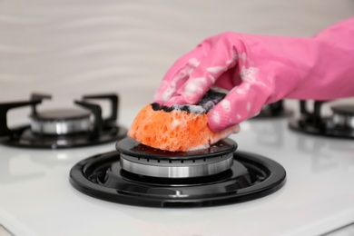 Person cleaning gas stove with sponge, closeup