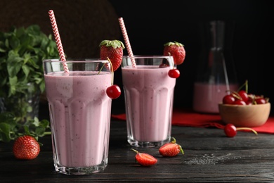 Photo of Tasty fresh milk shakes with berries on black wooden table. Space for text