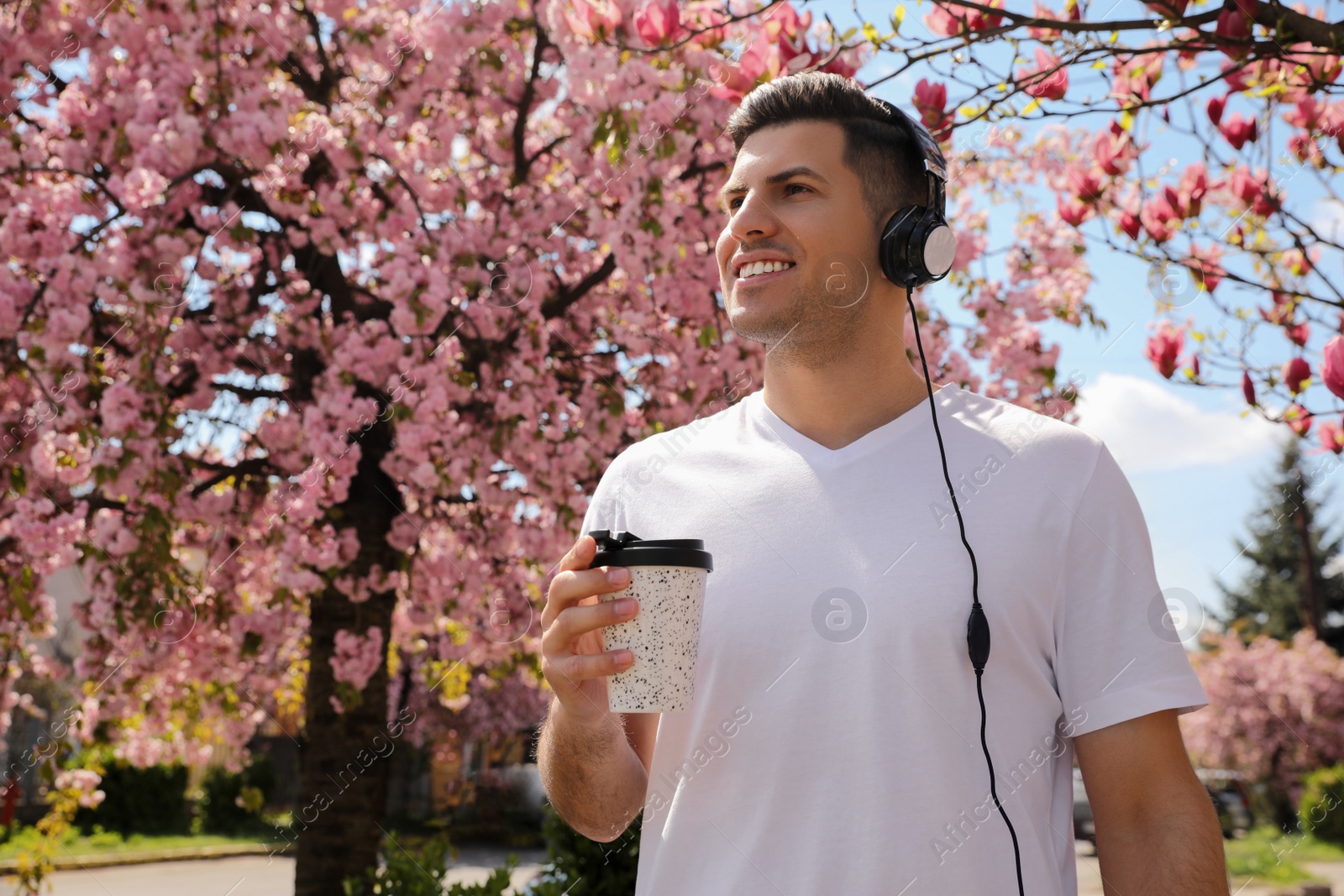 Photo of Happy man with coffee listening to audiobook outdoors on spring day