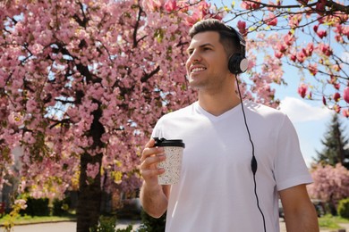 Happy man with coffee listening to audiobook outdoors on spring day