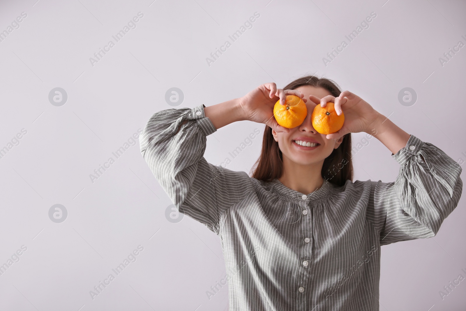 Photo of Woman with fresh tangerines on light grey background. Space for text