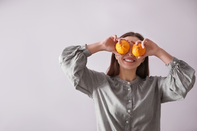 Woman with fresh tangerines on light grey background. Space for text