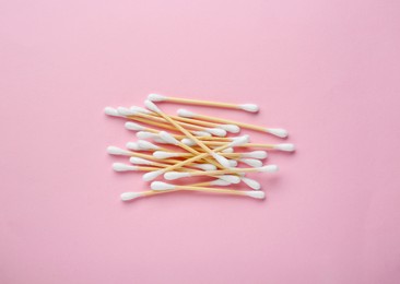 Heap of wooden cotton buds on pink background, flat lay