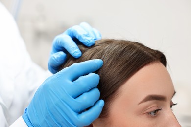 Photo of Trichologist examining patient`s hair under lamp in clinic, closeup