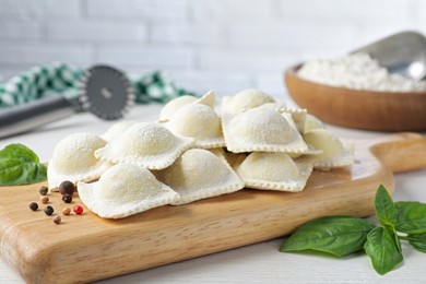 Photo of Uncooked ravioli, peppercorns and basil on white wooden table, closeup