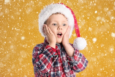 Image of Cute child in Santa hat under snowfall on yellow background. Christmas celebration