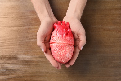 Photo of Man holding model of heart on wooden table. Heart attack concept