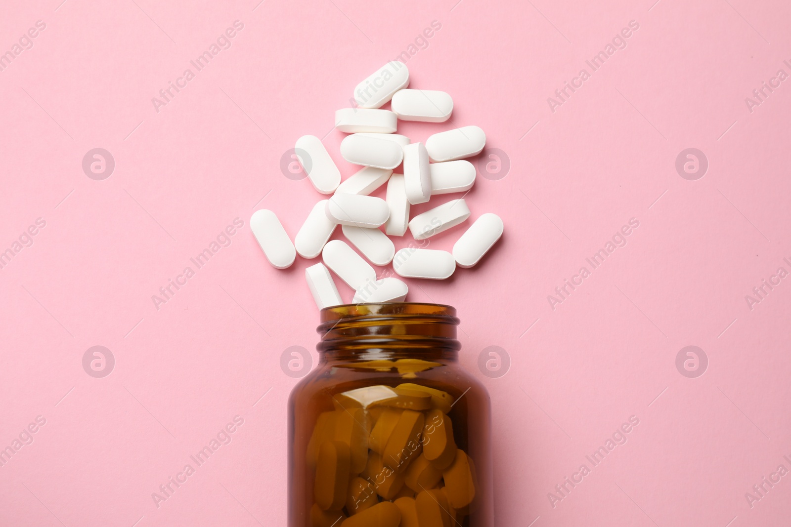 Photo of Bottle and vitamin capsules on pink background, top view