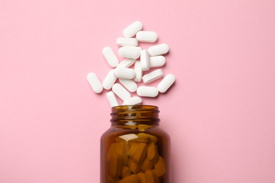 Bottle and vitamin capsules on pink background, top view