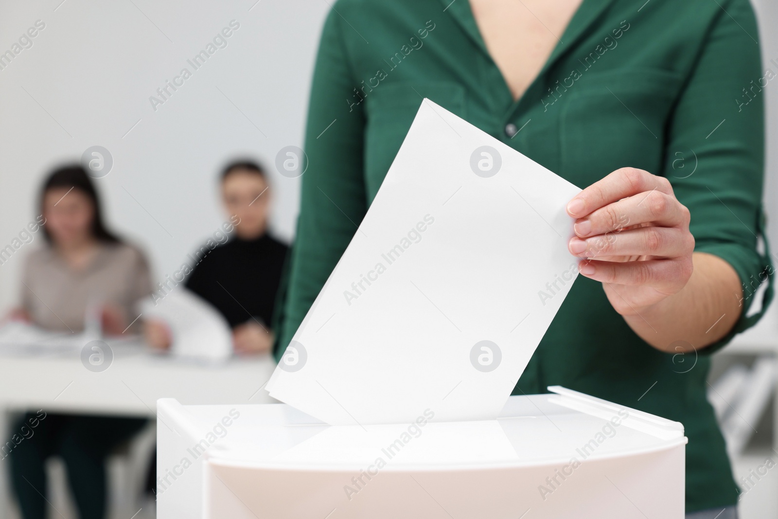 Photo of Woman putting her vote into ballot box on blurred background, closeup