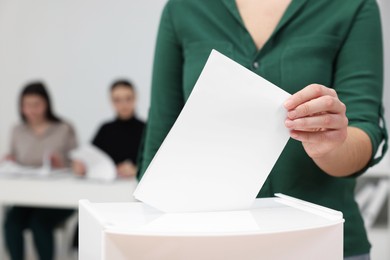 Woman putting her vote into ballot box on blurred background, closeup