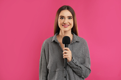 Photo of Young female journalist with microphone on pink background