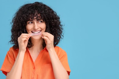 Photo of Young woman applying whitening strip on her teeth against light blue background, space for text