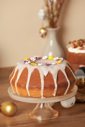 Photo of Delicious Easter cake decorated with sprinkles near painted eggs on wooden table