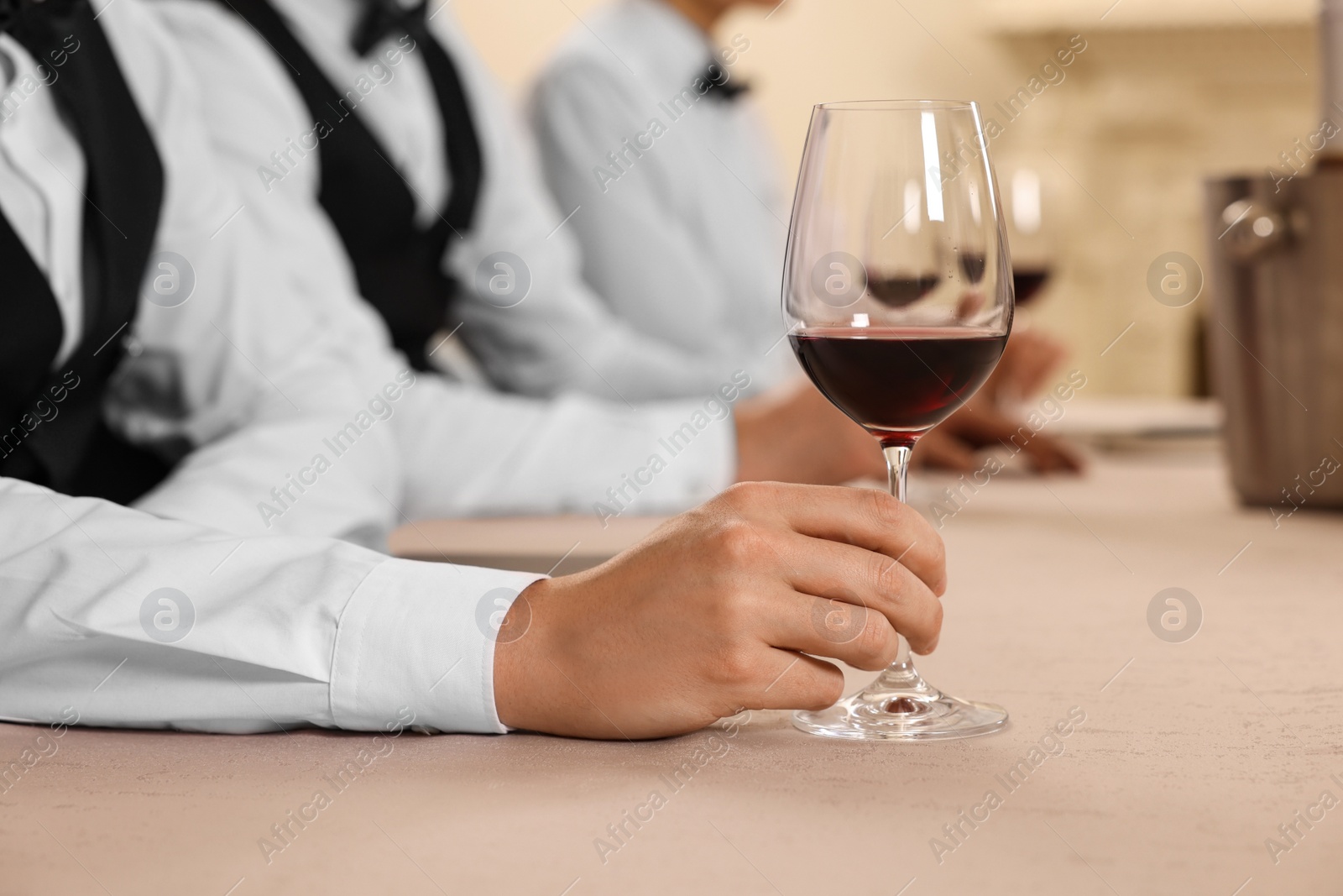 Photo of People with glasses of red wine at table indoors, closeup. Professional butler courses