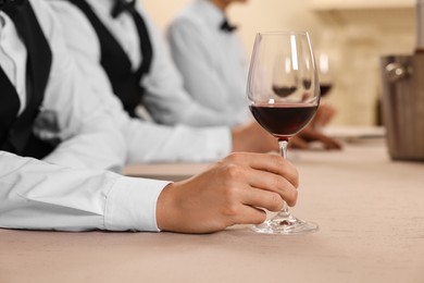 Photo of People with glasses of red wine at table indoors, closeup. Professional butler courses