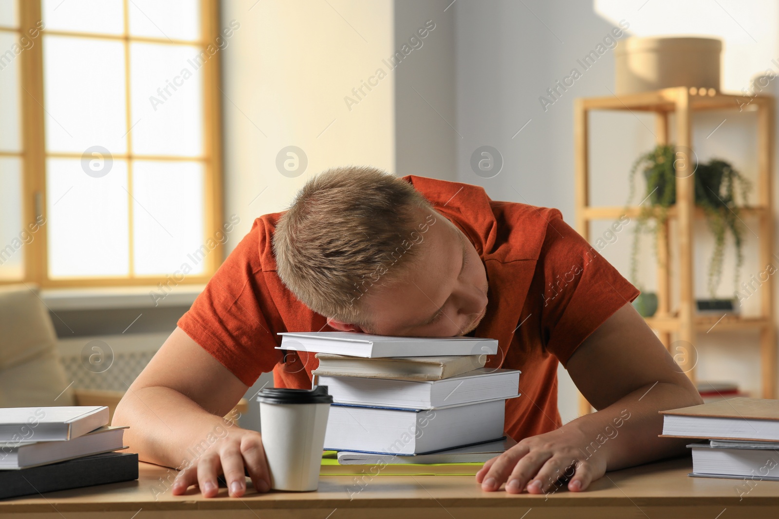 Photo of Tired man sleeping near books at wooden table indoors