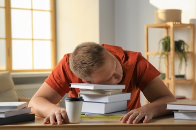 Tired man sleeping near books at wooden table indoors