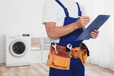 Plumber with clipboard and tool belt indoors, closeup. Space for text