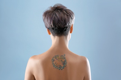 Photo of Beautiful tattoo on female back against color background