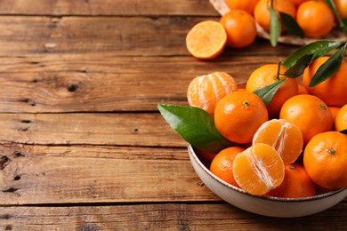 Photo of Fresh tangerines with green leaves in bowl on wooden table, space for text