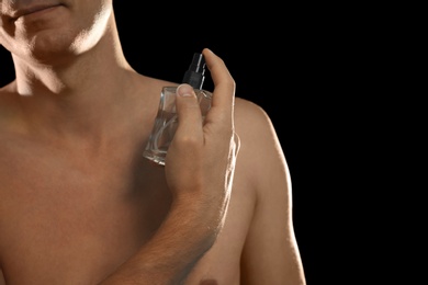 Photo of Young man using perfume on black background, closeup