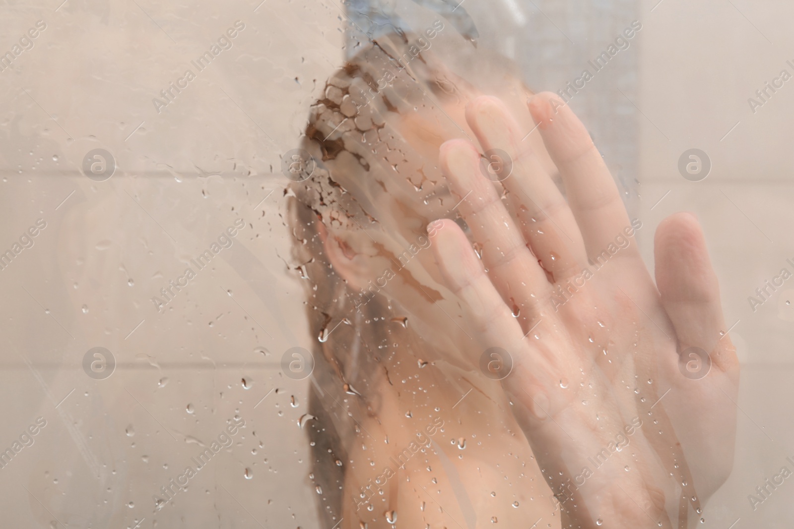 Photo of Young woman taking shower, view through glass door