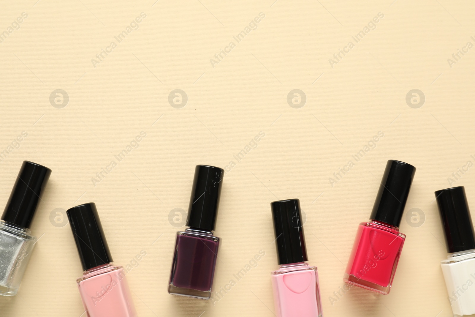 Photo of Bright nail polishes in bottles on beige background, flat lay. Space for text