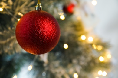 Photo of Beautiful red holiday bauble hanging on Christmas tree against blurred fairy lights, closeup. Space for text