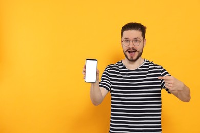 Emotional man pointing at smartphone on orange background. Space for text