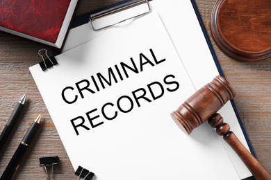 Clipboard with words CRIMINAL RECORD and gavel on wooden table, flat lay